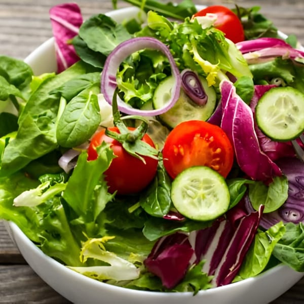 Close-up of a fresh garden salad with mixed greens, tomatoes, cucumbers, and red onion.