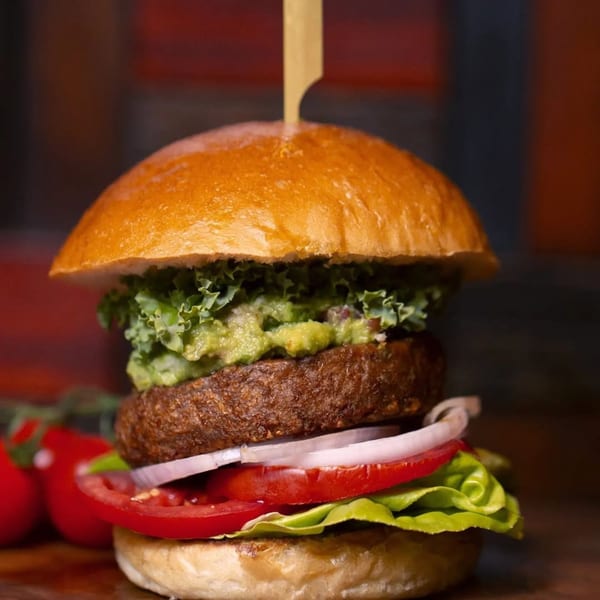 Burganic Hub's burger with a thick patty, guacamole, lettuce, tomato, and onion on a bun.