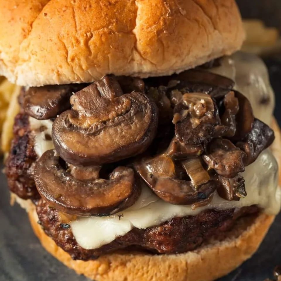 Close-up of a Burganic Hub mushroom and Swiss burger with a toasted bun.