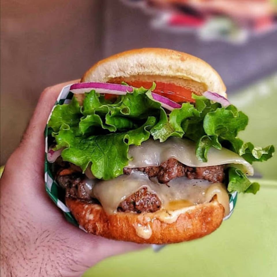 Hand holding a Burganic Hub double cheeseburger with lettuce, tomato, and red onion.