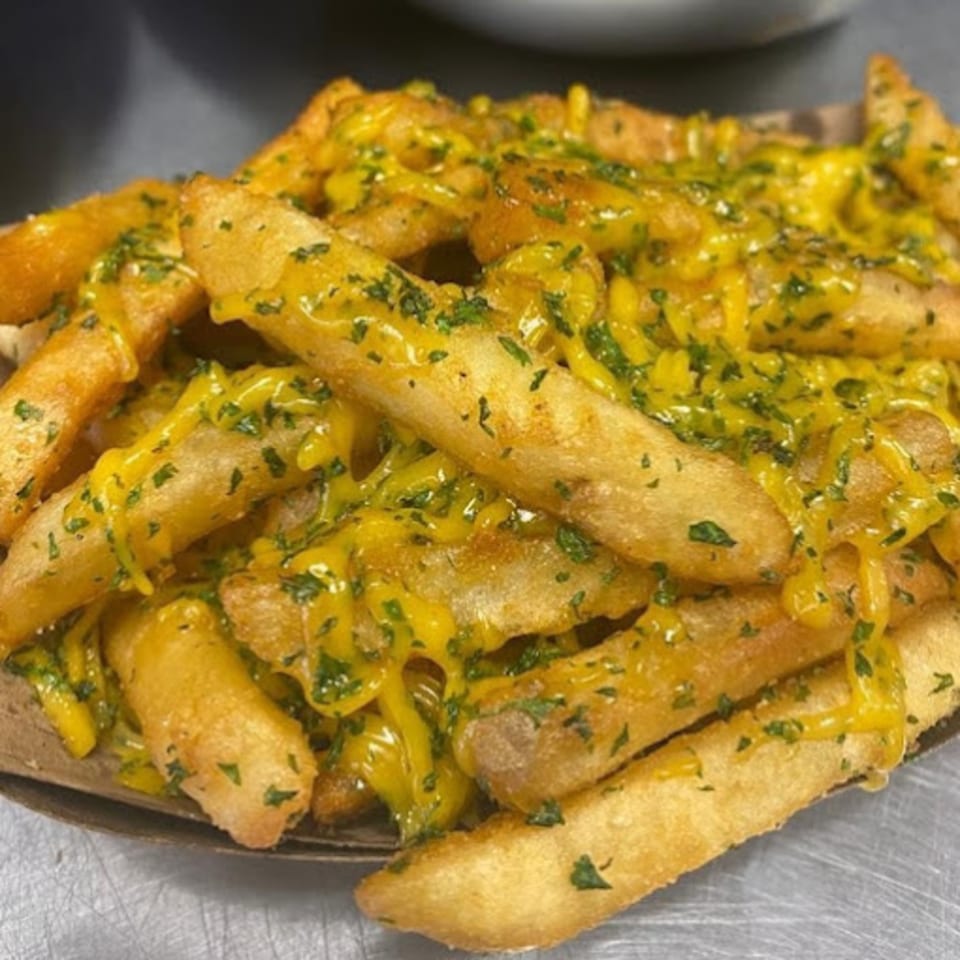 Golden-brown Burganic Hub fries generously topped with melted cheese and fresh green herbs.