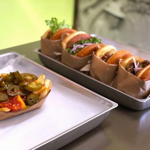 Burganic Hub sliders in paper wraps and jalapeño cheese fries on metal trays.